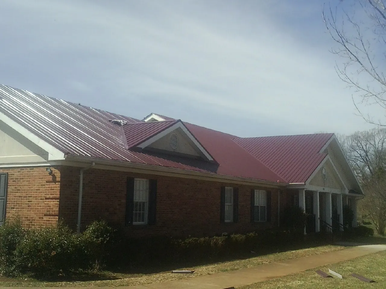 Red metal roof with gabled entries on a long brick building, from a Hail Damage Roof Repair job in Kahlotus