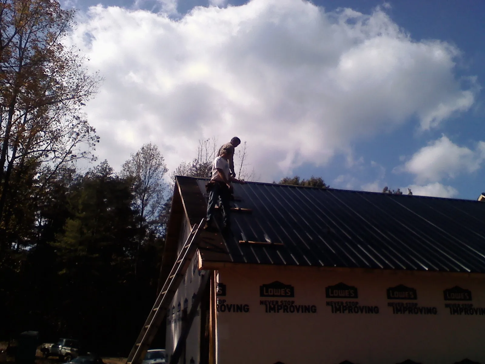 Roofer fastening dark metal panels high against a cloudy sky, from a Roof Inspection job in Kahlotus