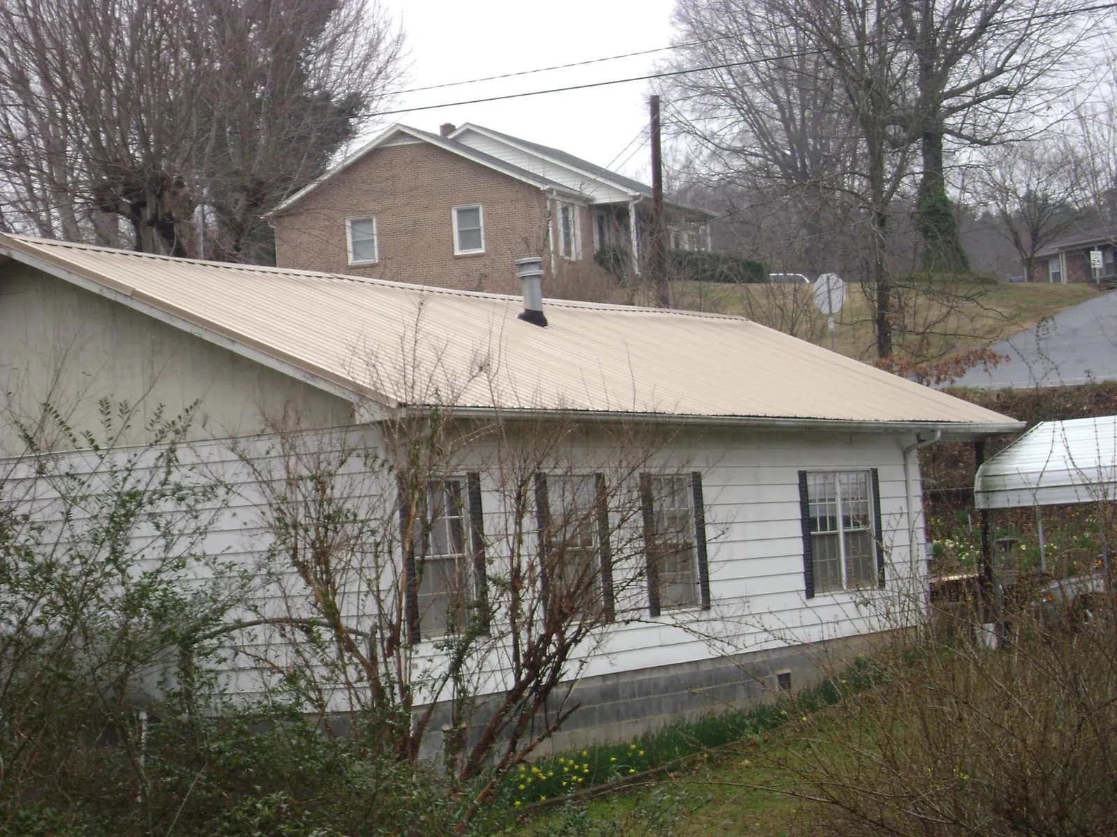 Tan metal roof on a white sided house set into a hillside — Commercial Roofing by Roofing Brothers in Kahlotus